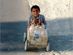 طفل يدفع عربه مليئة بزجاجات المياه