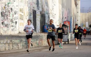 متسابقون يركضون بجانب جدار الفصل العنصري خلال ماراثون فلسطين الدولي الثامن في مدينة بيت لحم