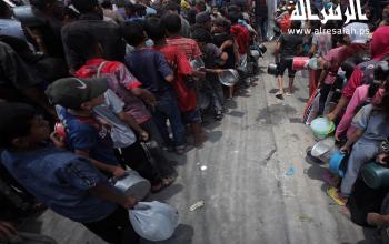 نازحون ينتظرون في طوابير للحصول على طعام مجاني من تكية خيرية في مخيم النصيرات وسط قطاع غزة