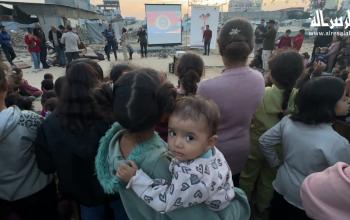 أطفال لاجئون يشاهدون الرسوم المتحركة في عرض أقيم لهم بالقرب من أنقاض المباني المدمرة وخيام النازحين في مدينة غزة